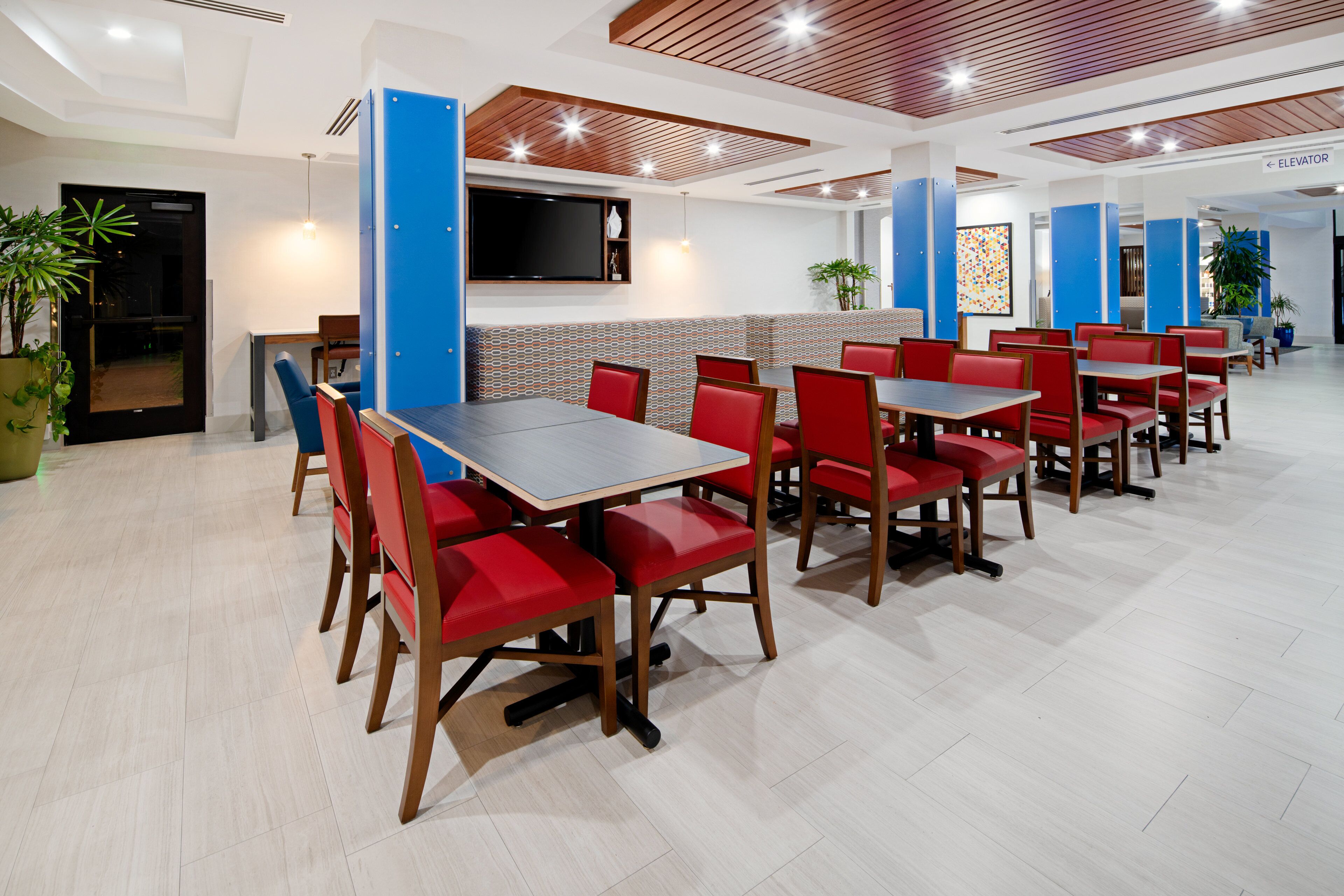A modern restaurant with red chairs and tables, a flat-screen TV, and a blue accent wall.