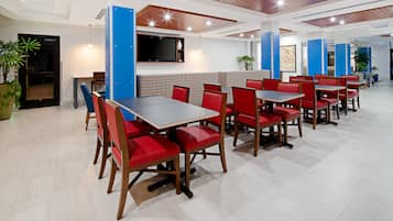 A modern restaurant with red chairs and tables, a flat-screen TV, and a blue accent wall.