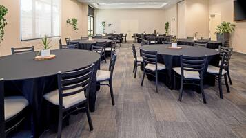 Un salón de conferencias con varias mesas redondas, sillas y plantas en macetas.