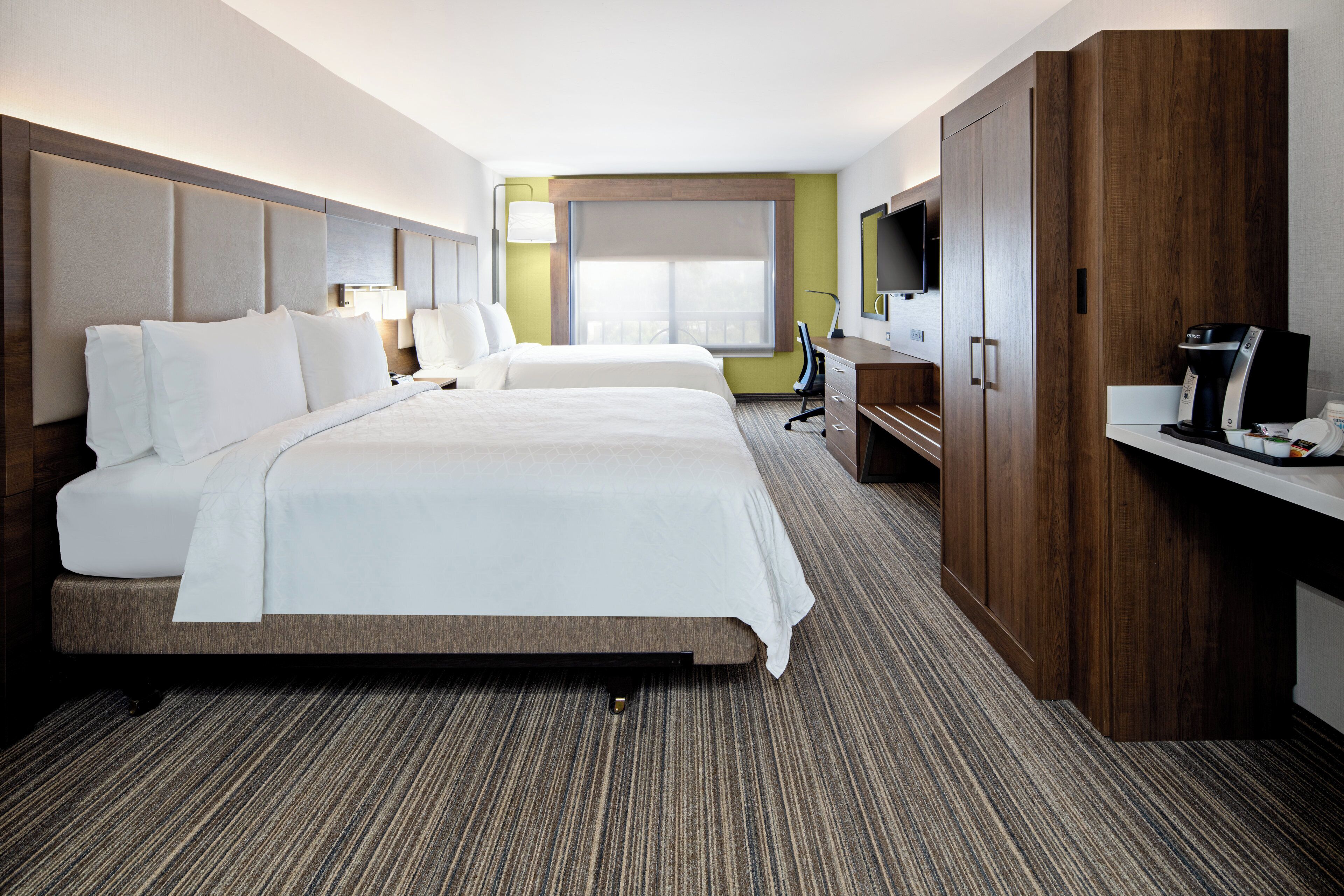 Habitación de hotel con una cama grande, un escritorio con cafetera, televisor y ventana con vistas.