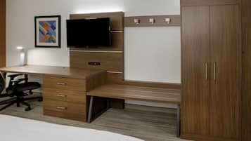 A hotel room with a wooden desk, a flat-screen TV, a wardrobe, and a bed.