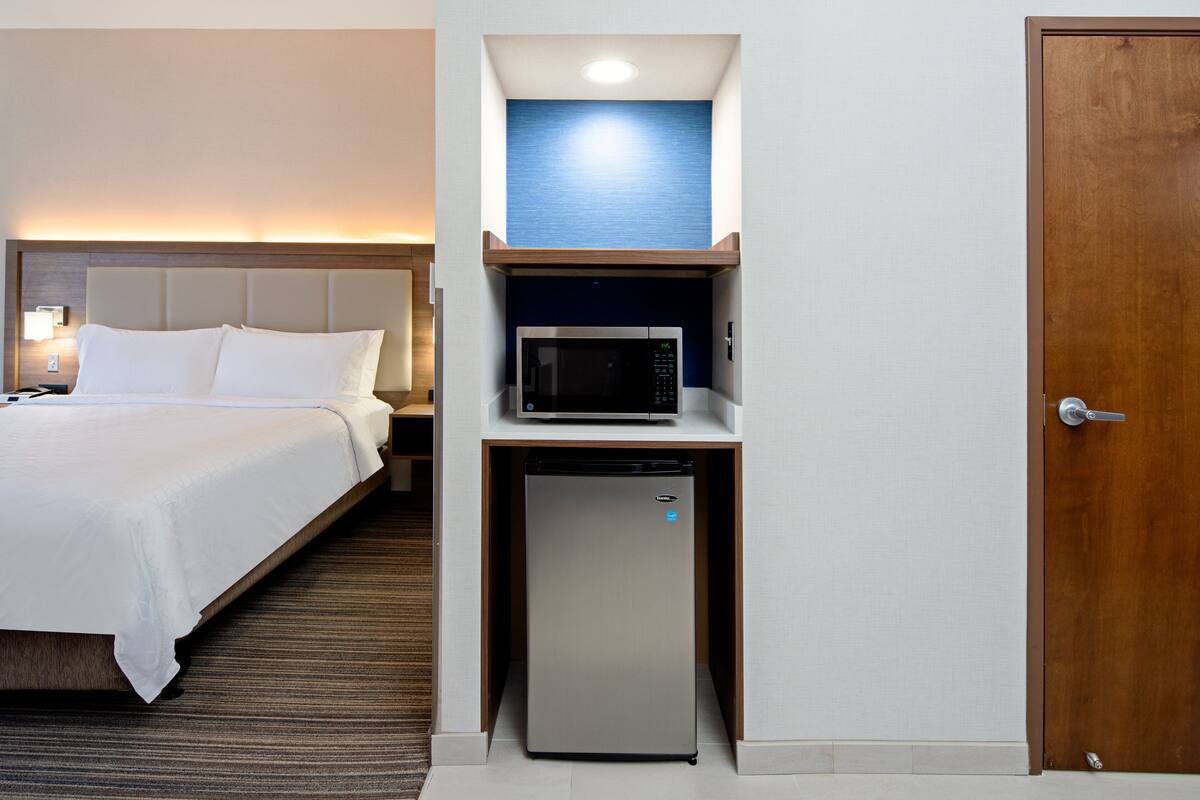 Ett hotellrum med en säng, en mikrovågsugn och ett kylskåp placerat under en hylla.