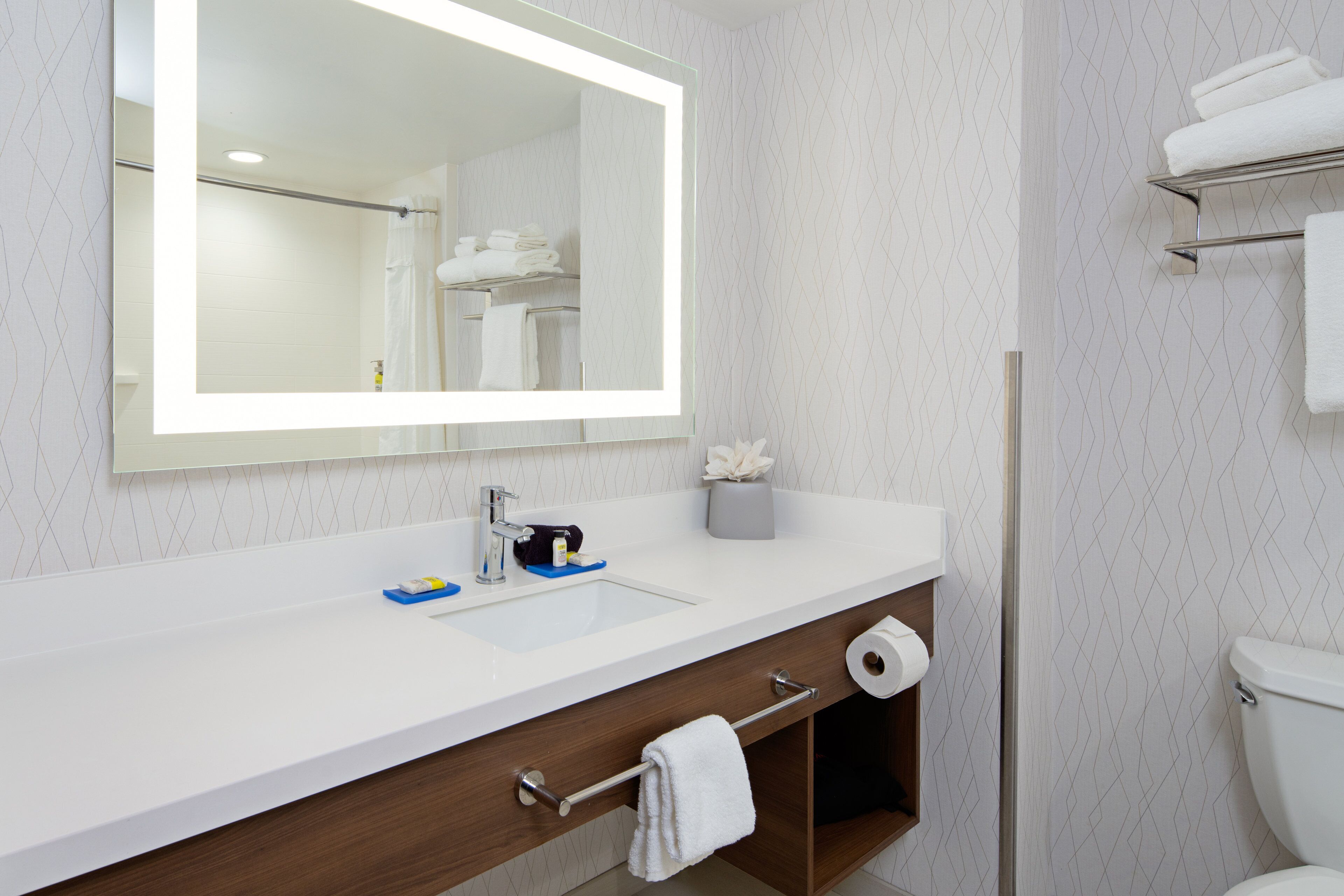 A modern bathroom with a large mirror, white sink, and a toilet.