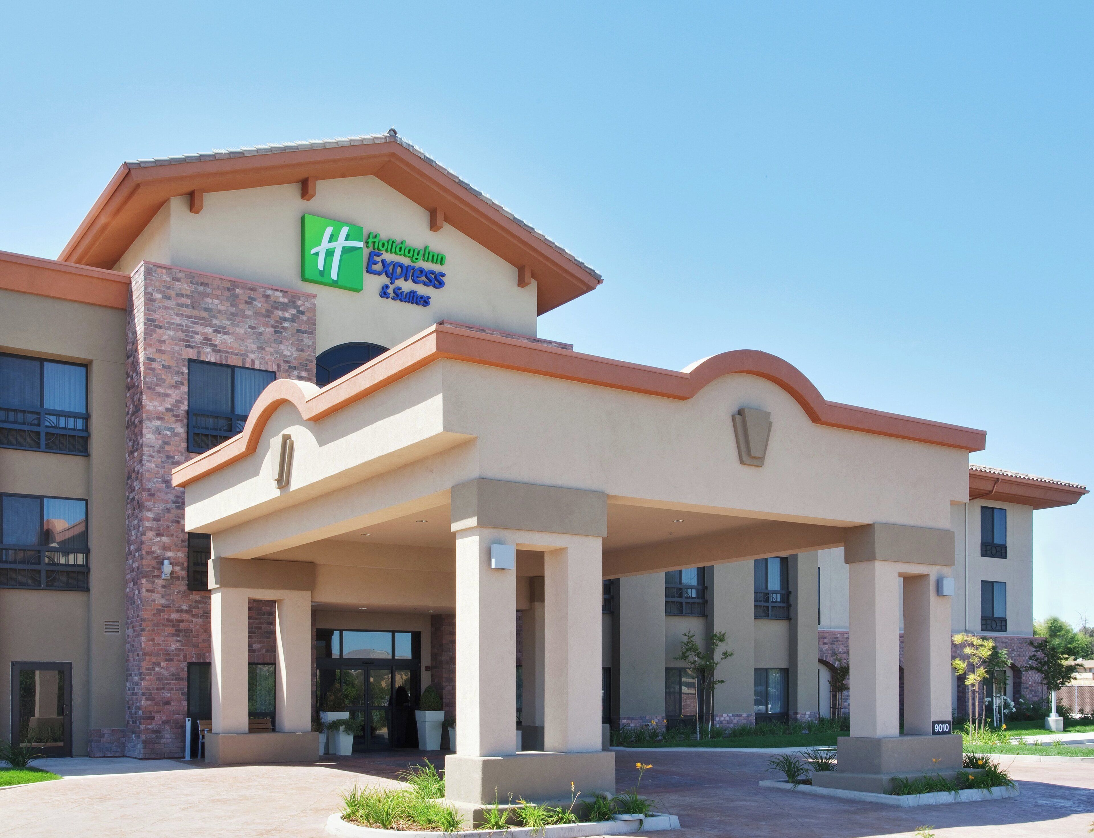 Un bâtiment de l’hôtel Holiday Inn Express avec une façade en briques, de grandes portes d’entrée et un espace extérieur couvert agrémenté de jardinières.
