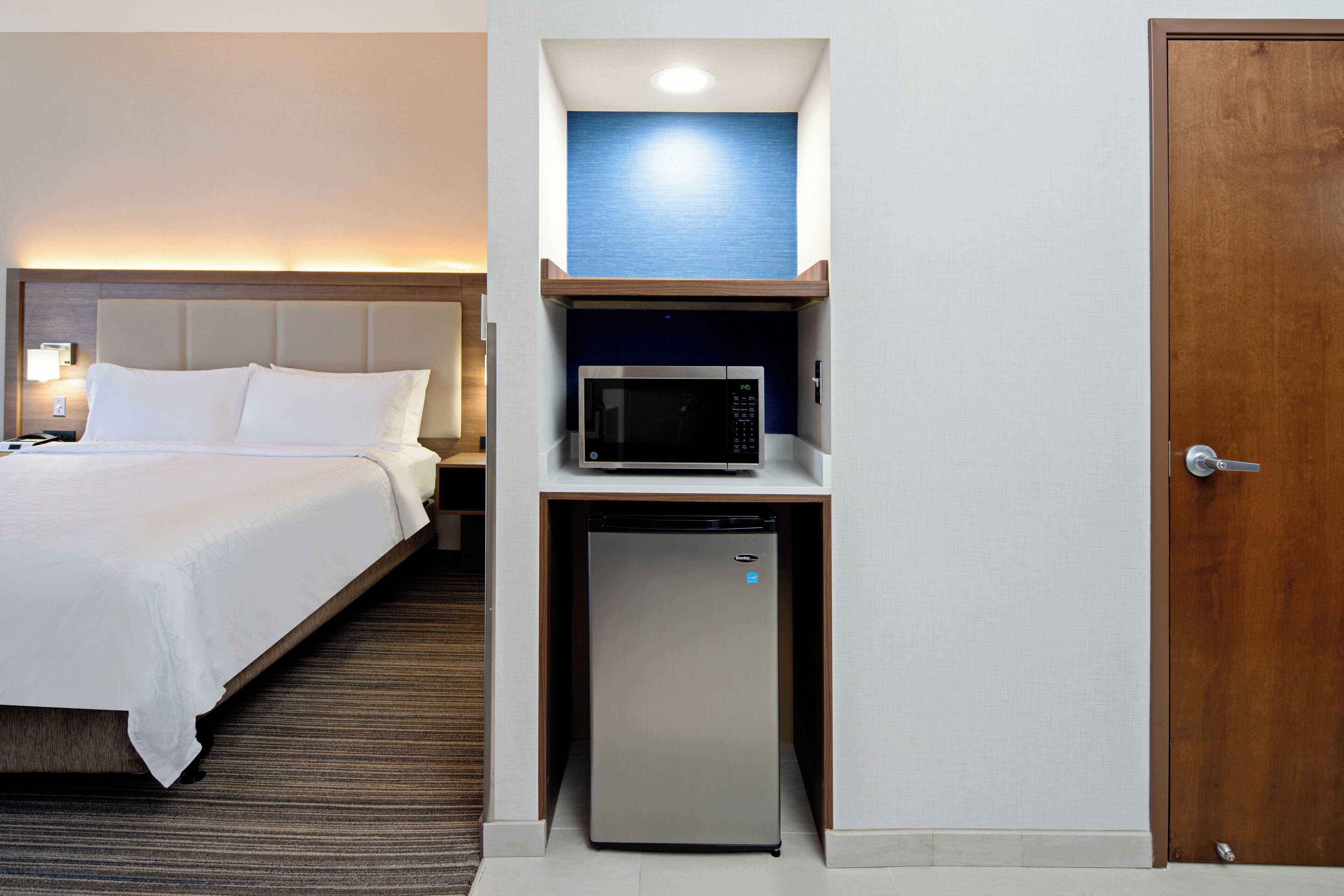 A hotel room with a bed, a microwave, and a refrigerator under a shelf.