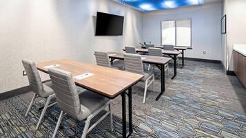 A conference room with a large table, chairs, a flat-screen TV, and a patterned carpet.