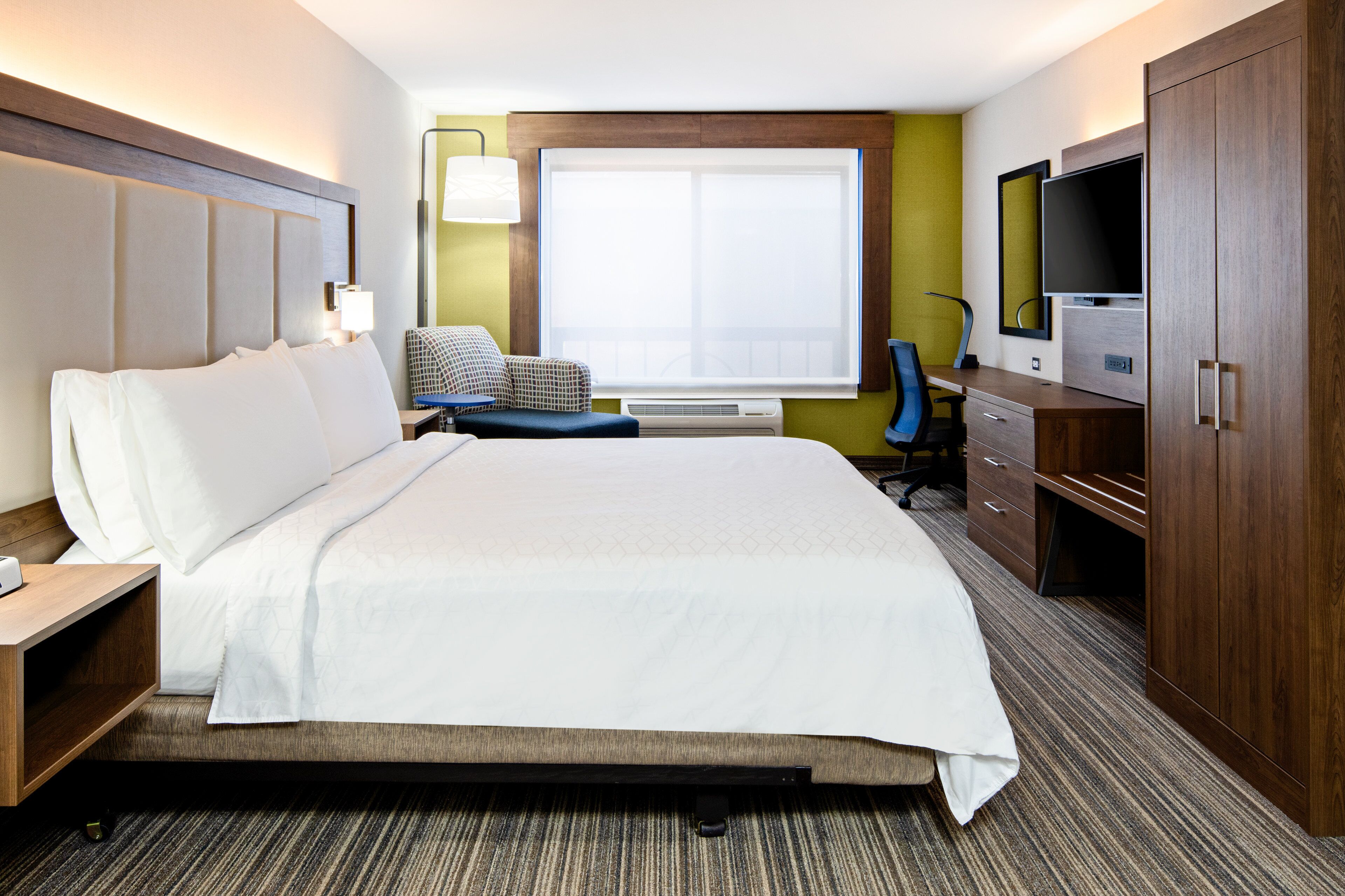 A hotel room with a large bed, a desk with a chair, a television, and a wardrobe.