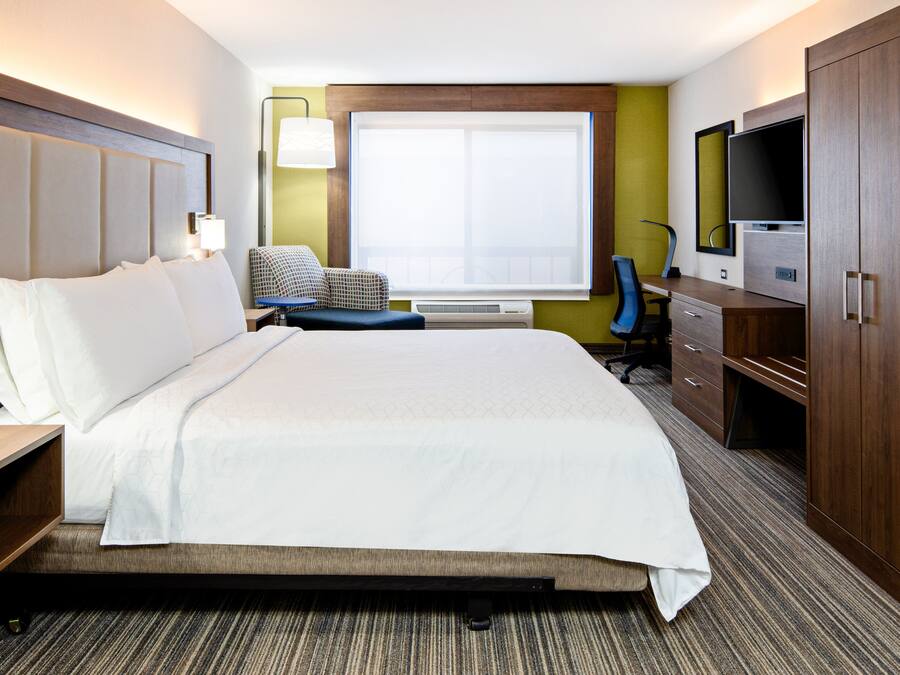 Habitación de hotel con una cama grande, un escritorio con silla, un televisor y un armario.