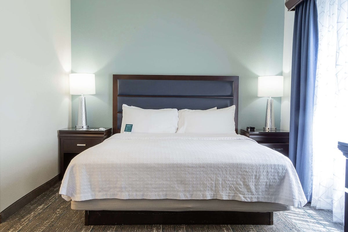 A neatly made bed with white linens, two bedside lamps, and a dark headboard in a hotel room.