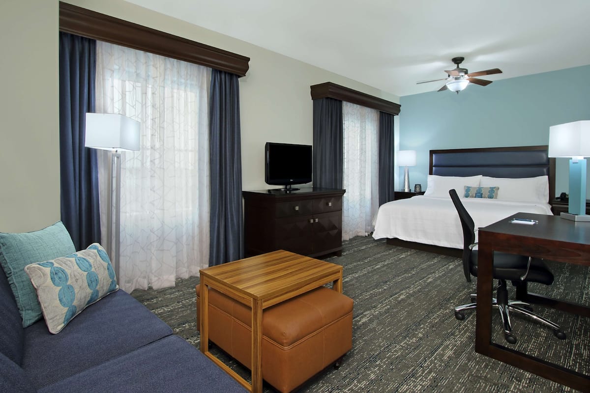 A hotel room with a bed, a desk, a chair, a TV, a dresser, and a sofa.