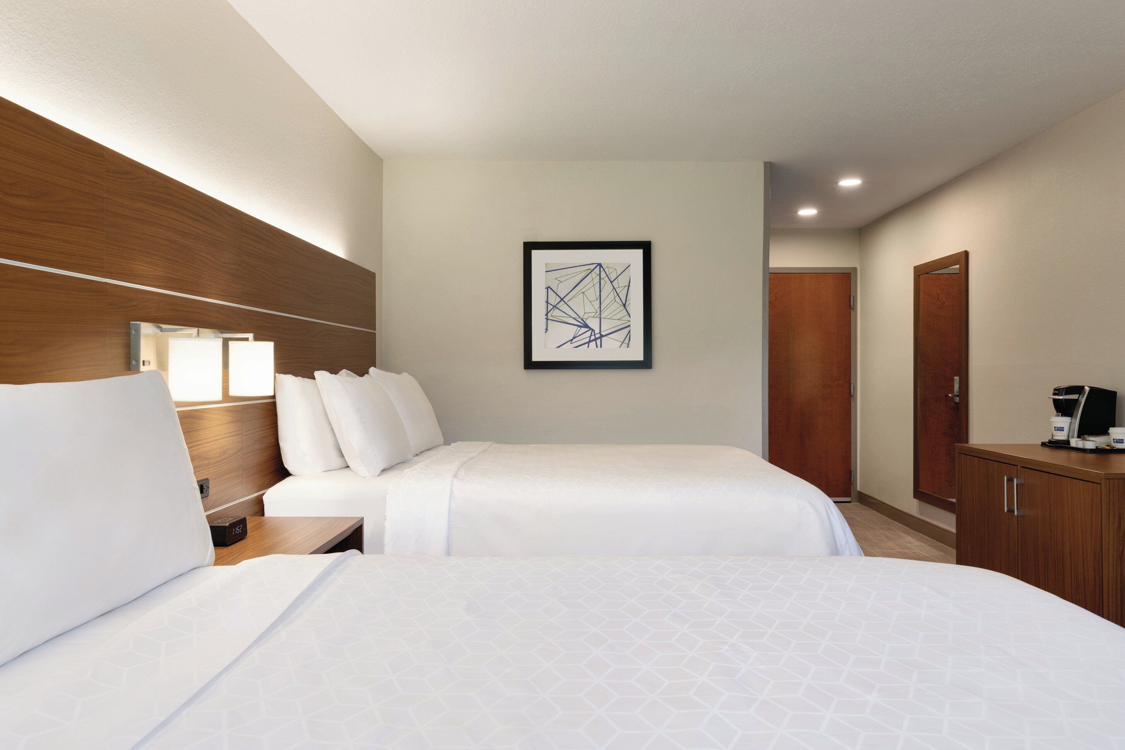 Habitación de hotel con dos camas, una mesita de noche, una obra de arte abstracta enmarcada, un armario de madera y una cafetera.