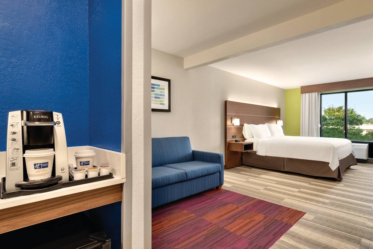 A hotel room with a bed, a sofa, a coffee machine, and a window with a view.