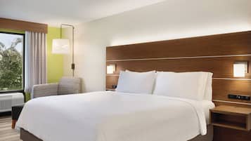 A hotel room with a large bed, a bedside table, a chair, and a window with curtains.