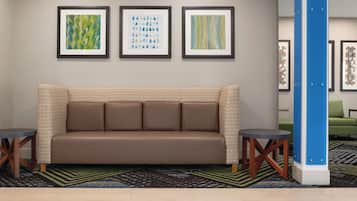A hotel lobby with a brown sofa, two side tables, and three framed artworks on the wall.