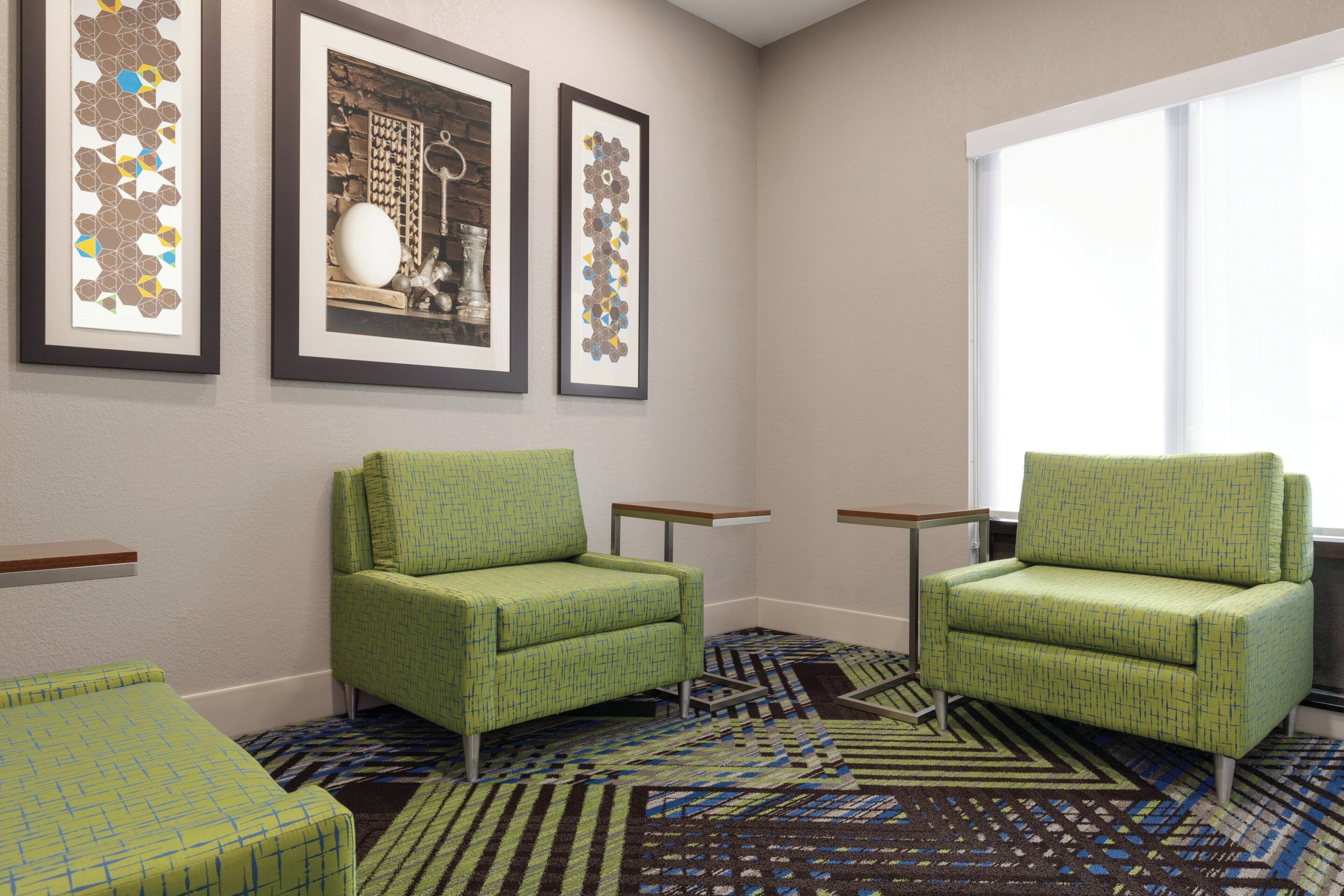 A room with two green armchairs, a patterned carpet, and three framed artworks on the wall.