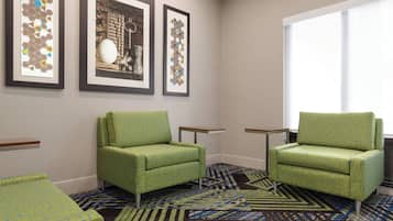 A room with two green armchairs, a patterned carpet, and three framed artworks on the wall.