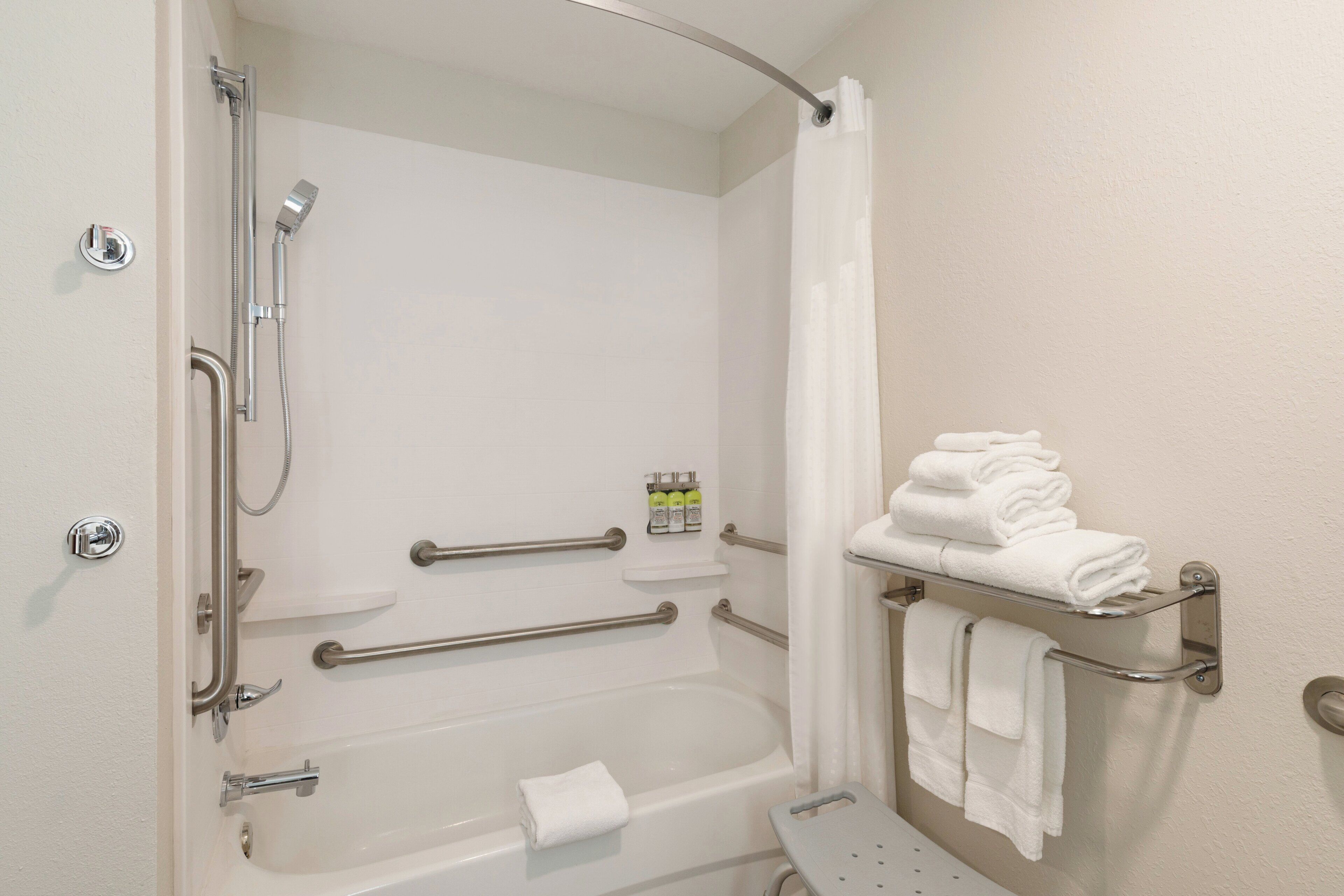 A bathroom with a walk-in shower, grab bars, a bathtub, and a towel rack.