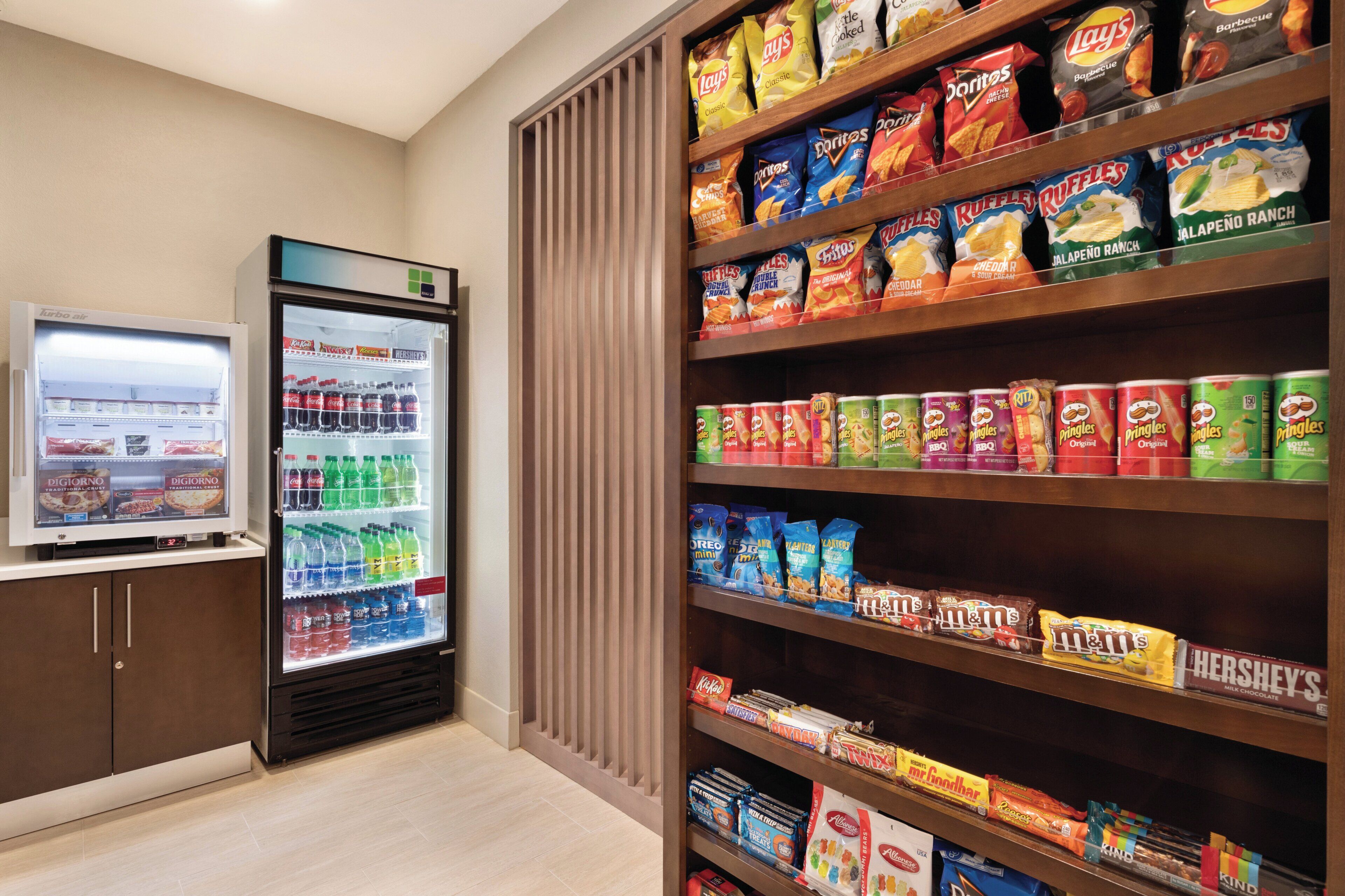 Zona de exhibición de bocadillos y bebidas con una variedad de papas fritas, refrescos y un refrigerador lleno de bebidas.