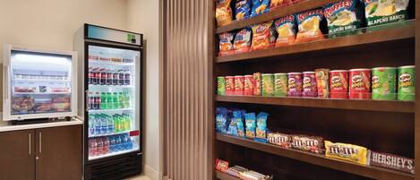 Zona de exhibición de bocadillos y bebidas con una variedad de papas fritas, refrescos y un refrigerador lleno de bebidas.