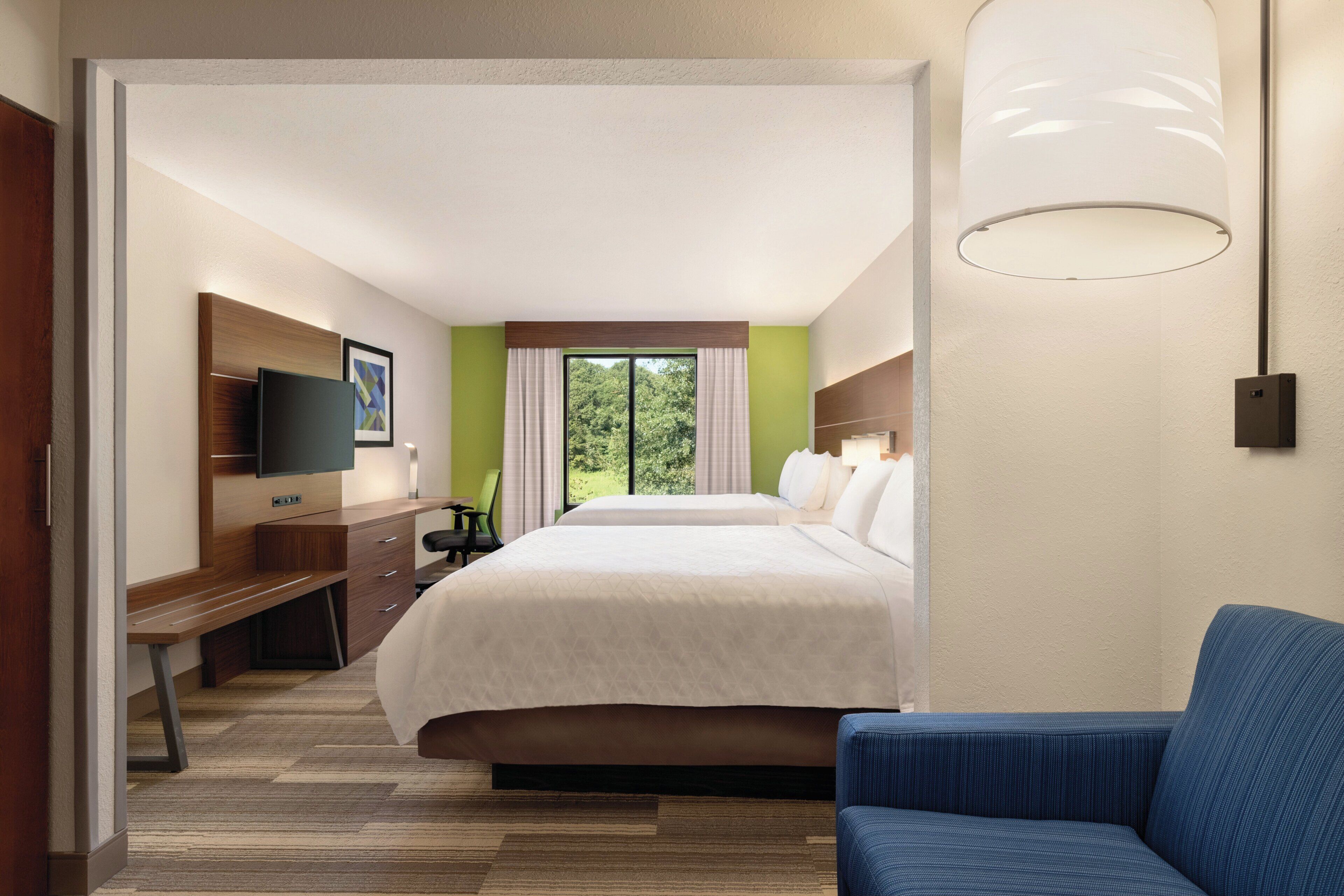 A hotel room with a bed, a desk, a chair, a television, and a window with curtains.