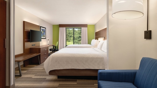 Habitación de hotel con una cama grande, un escritorio con silla, un televisor en la pared y un ventanal con cortinas.