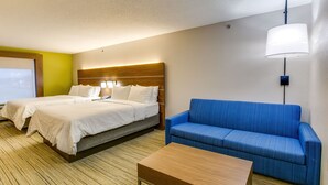 A hotel room with two beds, a blue sofa, and a wooden coffee table. - Holiday Inn Express Vincennes by IHG (Vincennes)