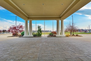 A covered outdoor area with a paved floor, columns, and a view of a park and distant buildings. - Holiday Inn Express Vincennes by IHG (Vincennes)