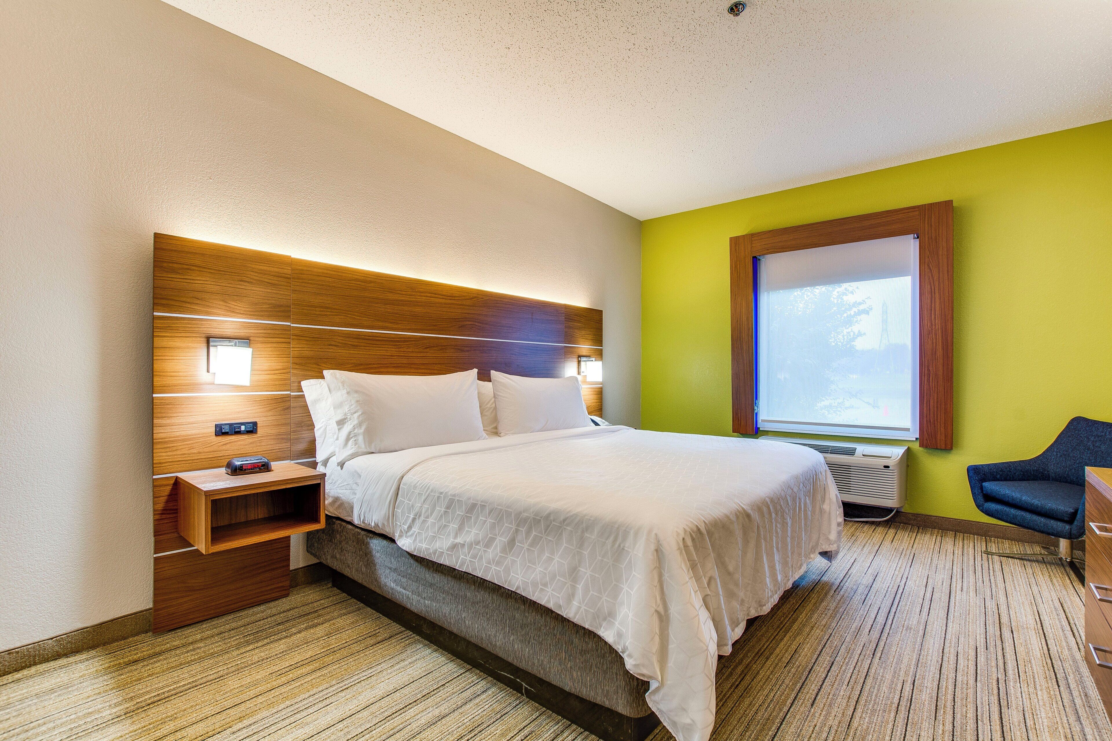 Habitación de hotel con cama, mesita de noche, lámpara y ventana con vistas.
