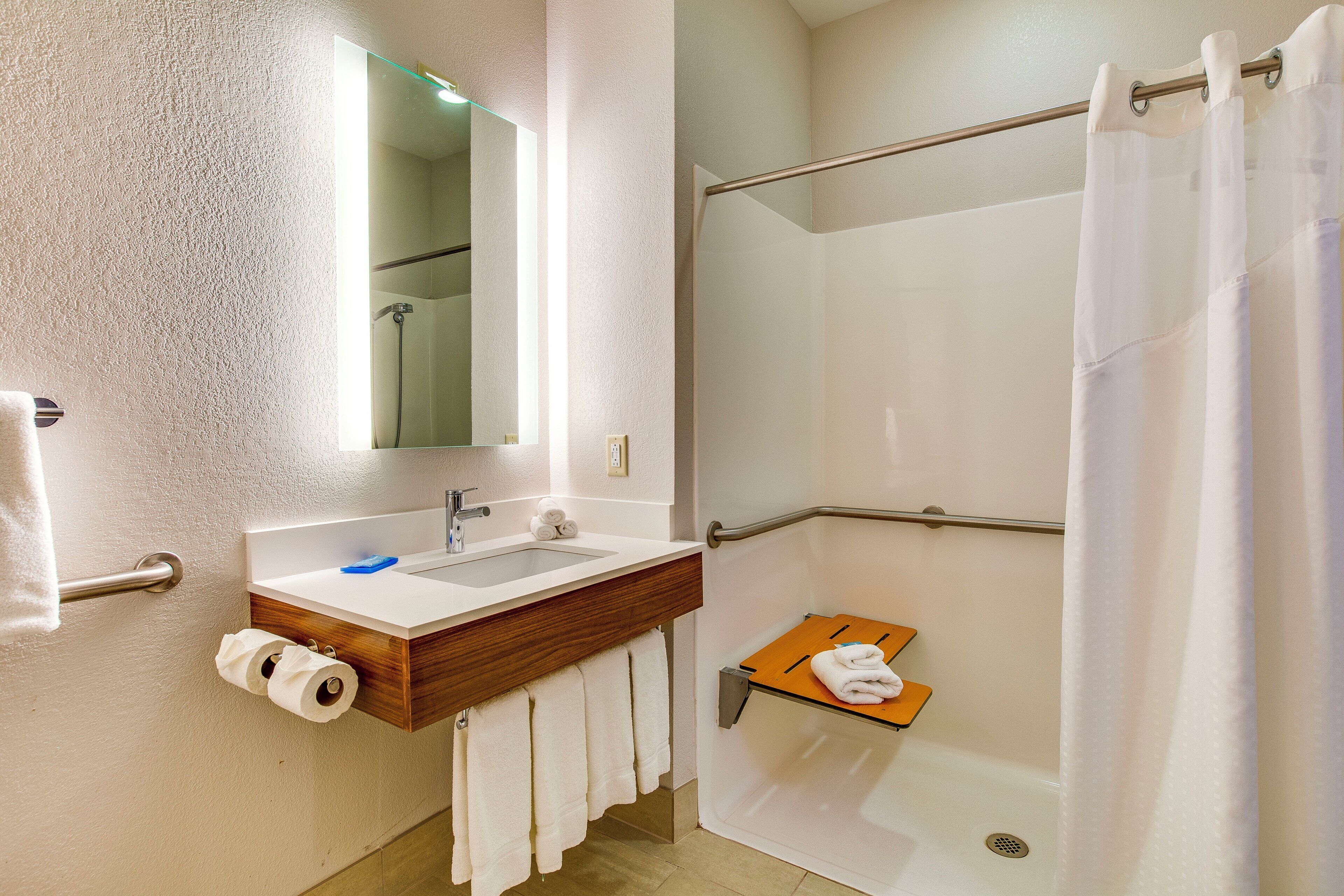 Un baño con lavamanos, espejo, toallero, ducha y un pequeño estante de madera.