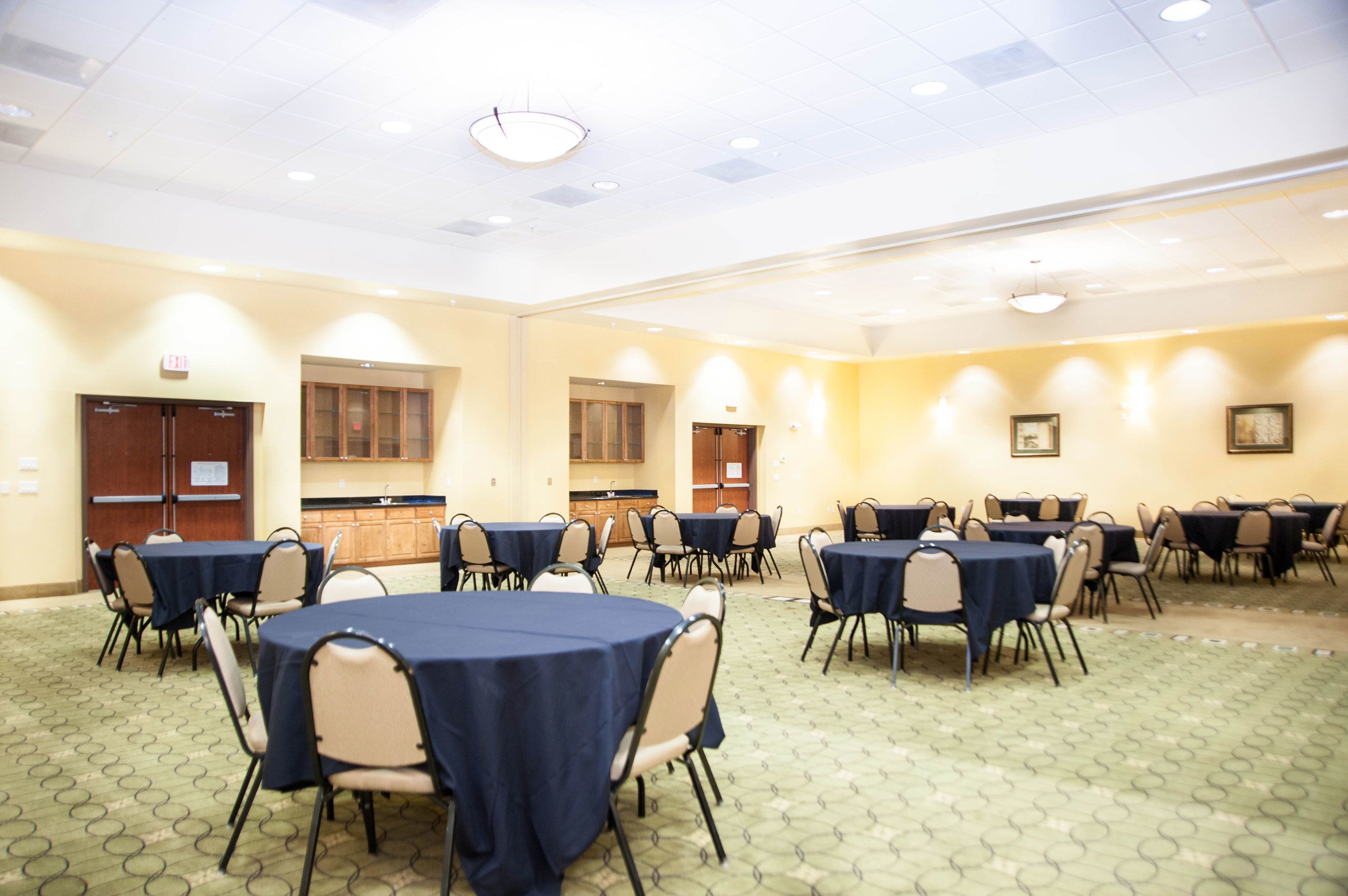A conference room with round tables, chairs, and a kitchenette area.