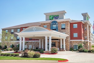 Un hotel Holiday Inn Express & Suites con entrada cubierta, fachada de ladrillo y bandera estadounidense.