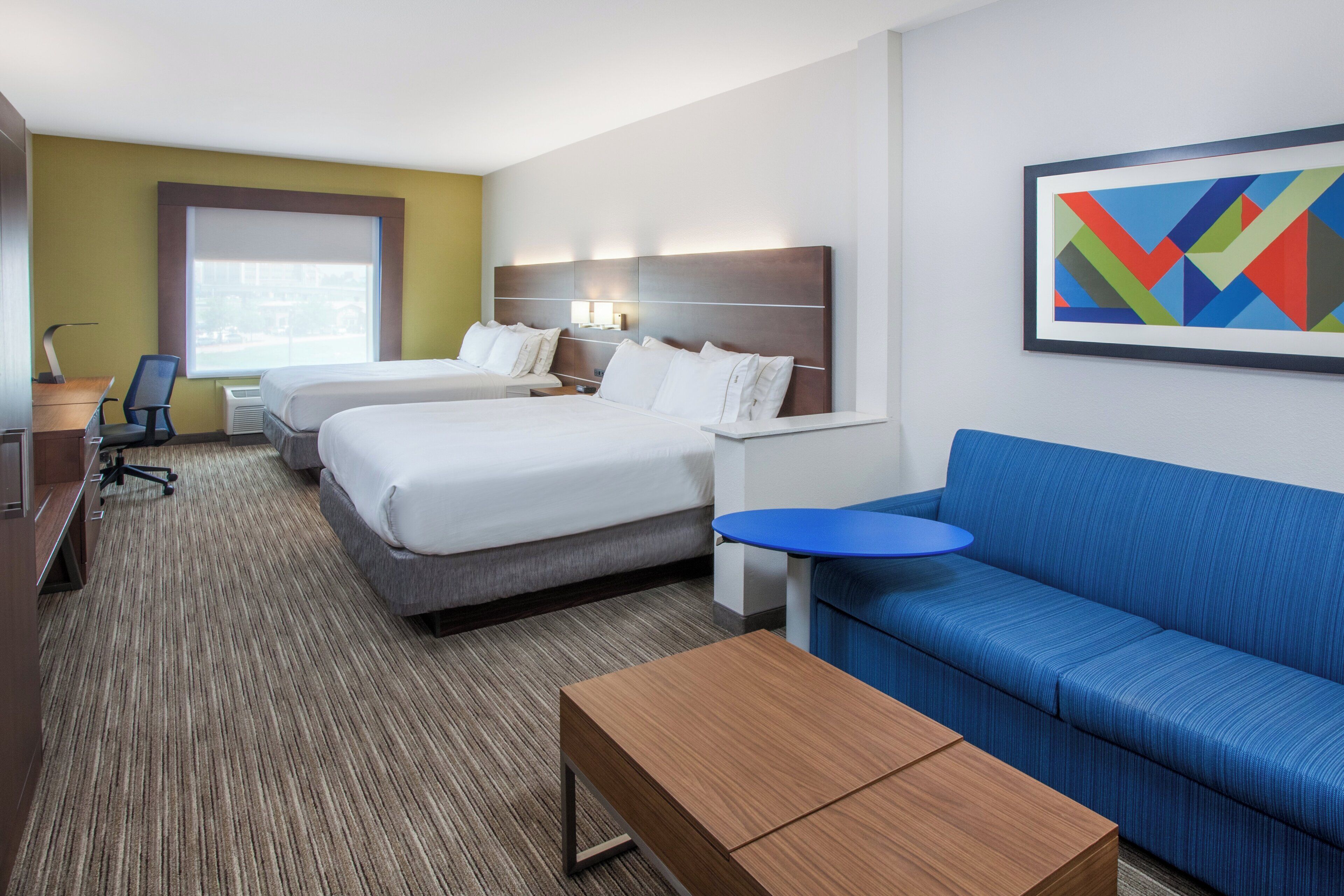 Una habitación de hotel con dos camas, un sofá azul, una mesita y un cuadro en la pared.