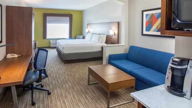 A hotel room with a bed, a desk with a chair, a coffee maker, a blue sofa, and a television. - Holiday Inn Express & Suites Texarkana by IHG (Texarkana)
