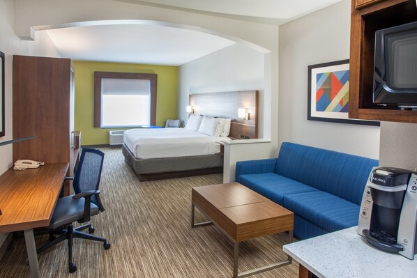 A hotel room with a bed, a desk with a chair, a coffee maker, a blue sofa, and a television. - Holiday Inn Express & Suites Texarkana by IHG (Texarkana)