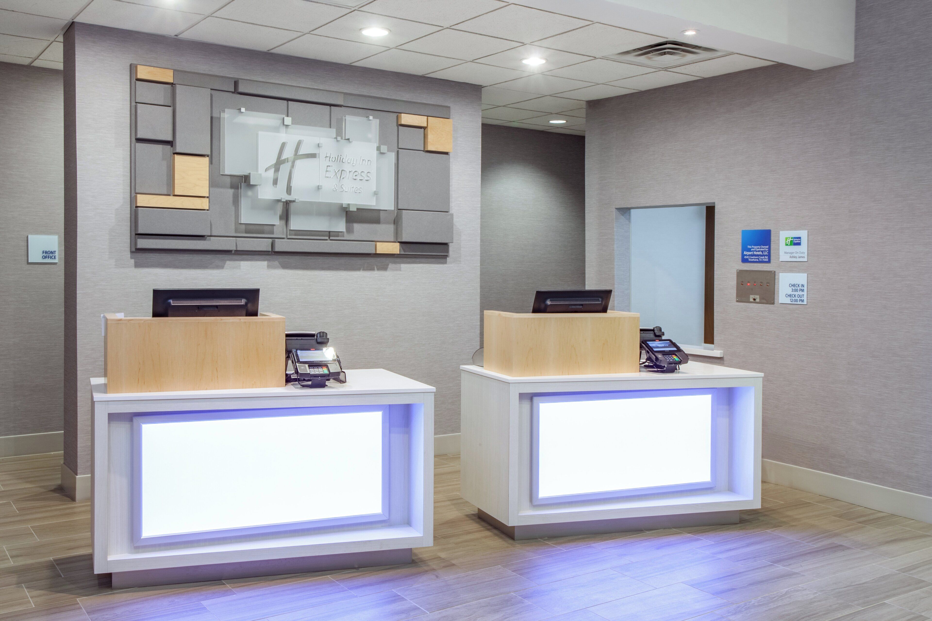 Zona de recepción de hotel con dos mostradores, un panel informativo en la pared y un quiosco de registro de entrada y salida.