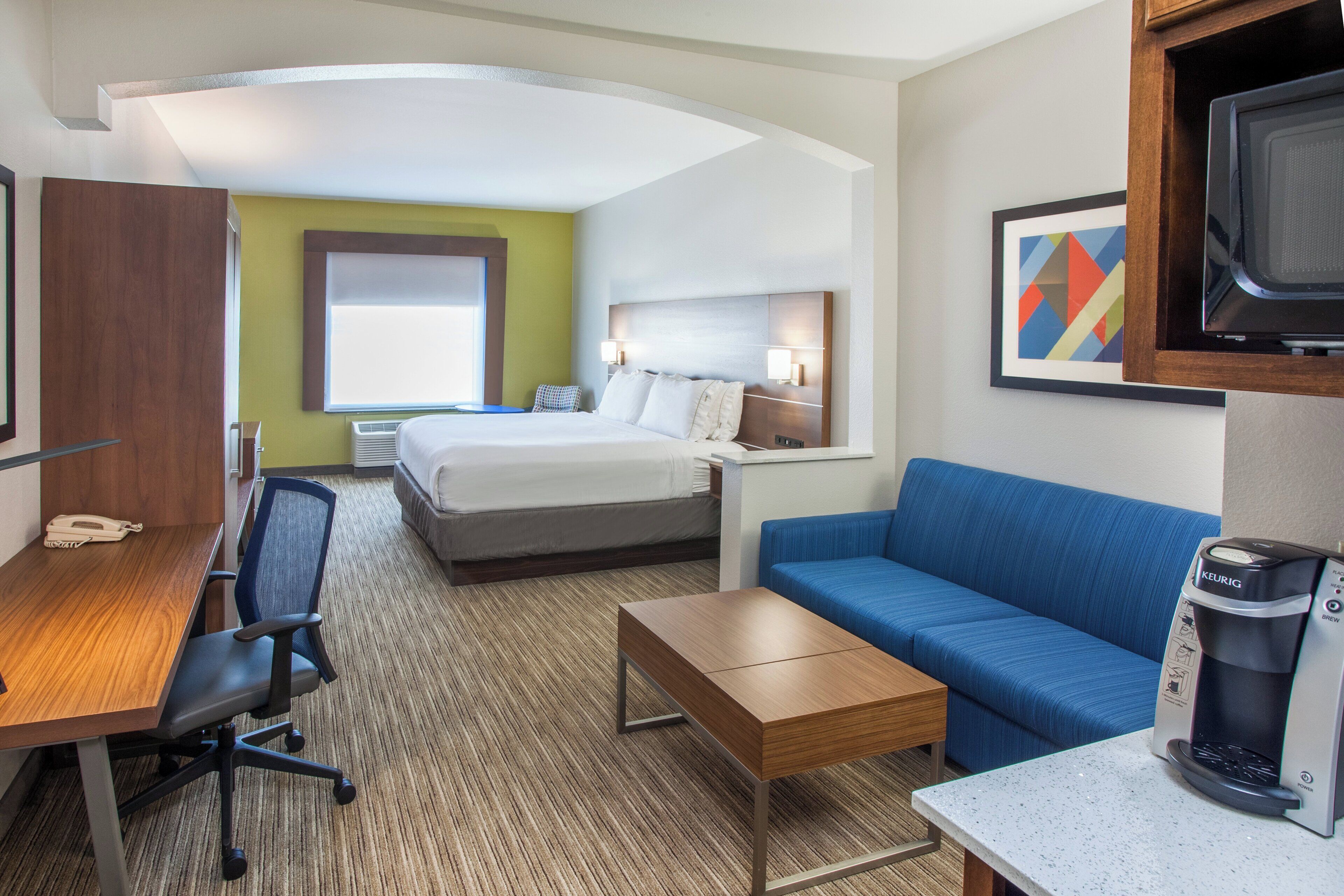 A hotel room with a bed, a desk, a chair, a coffee maker, and a television.