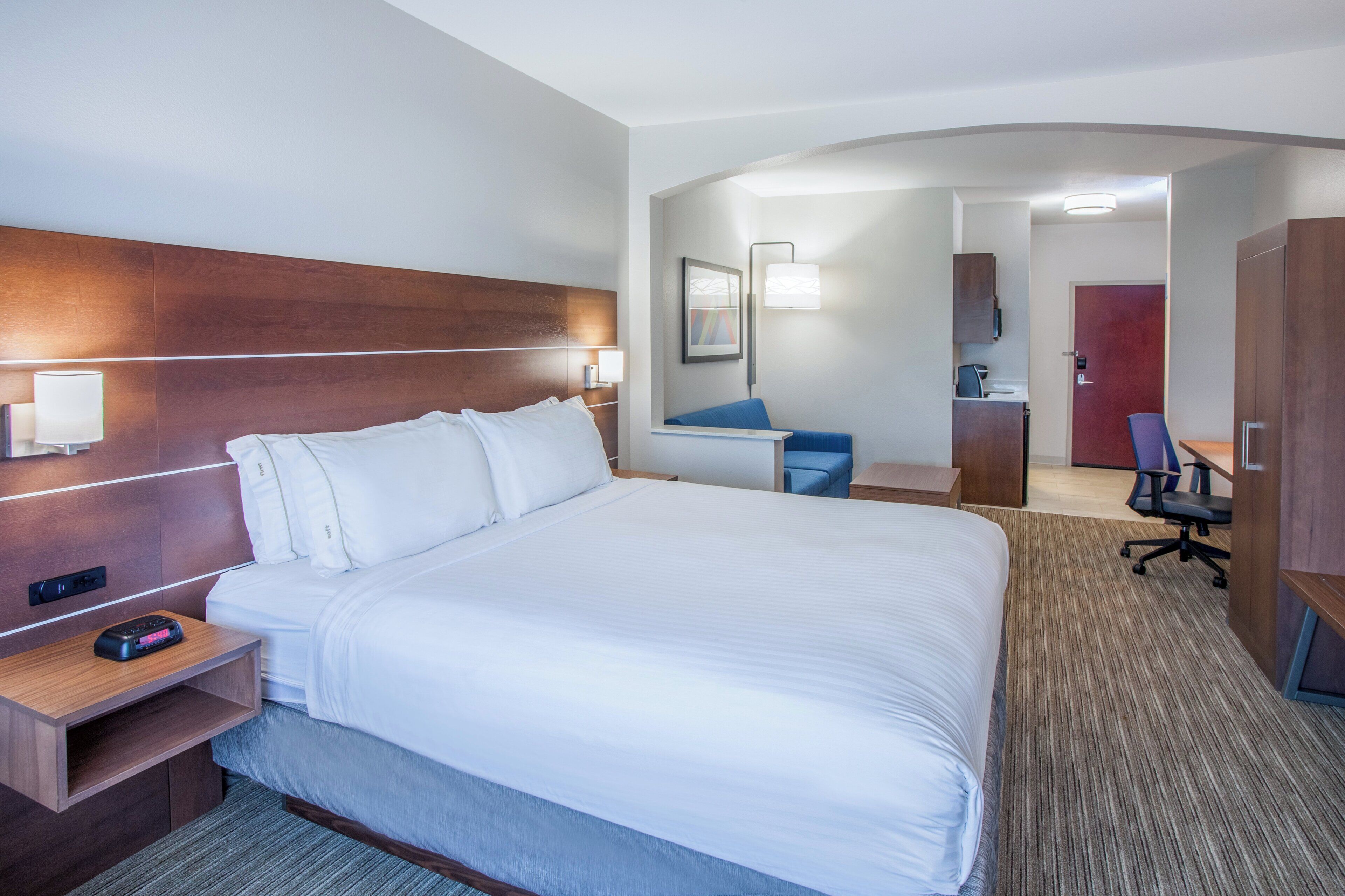 A hotel room with a large bed, bedside tables, a desk, a chair, and a wardrobe.