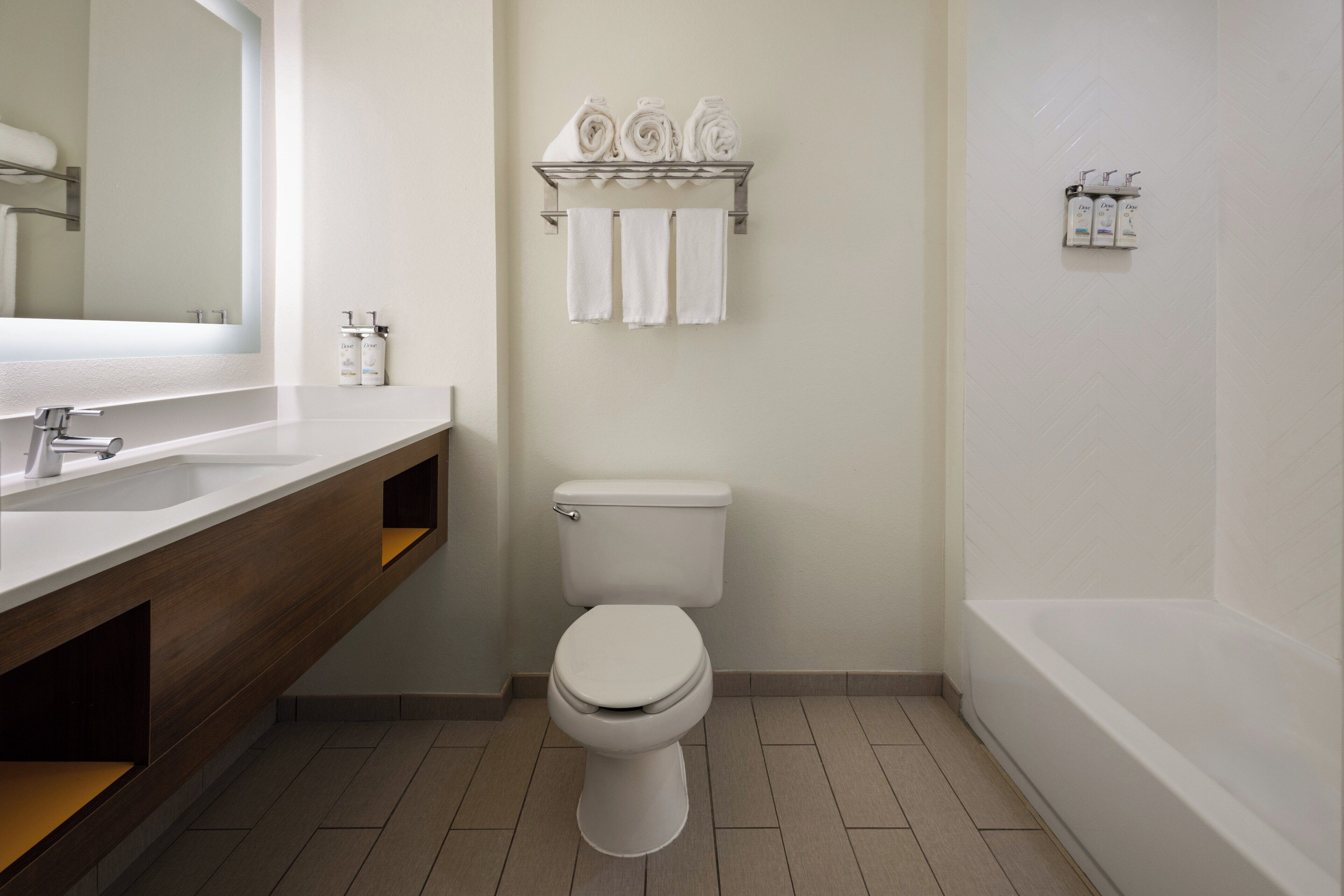 A modern bathroom with a white sink, toilet, and bathtub. There are towels and toiletries on the wall.