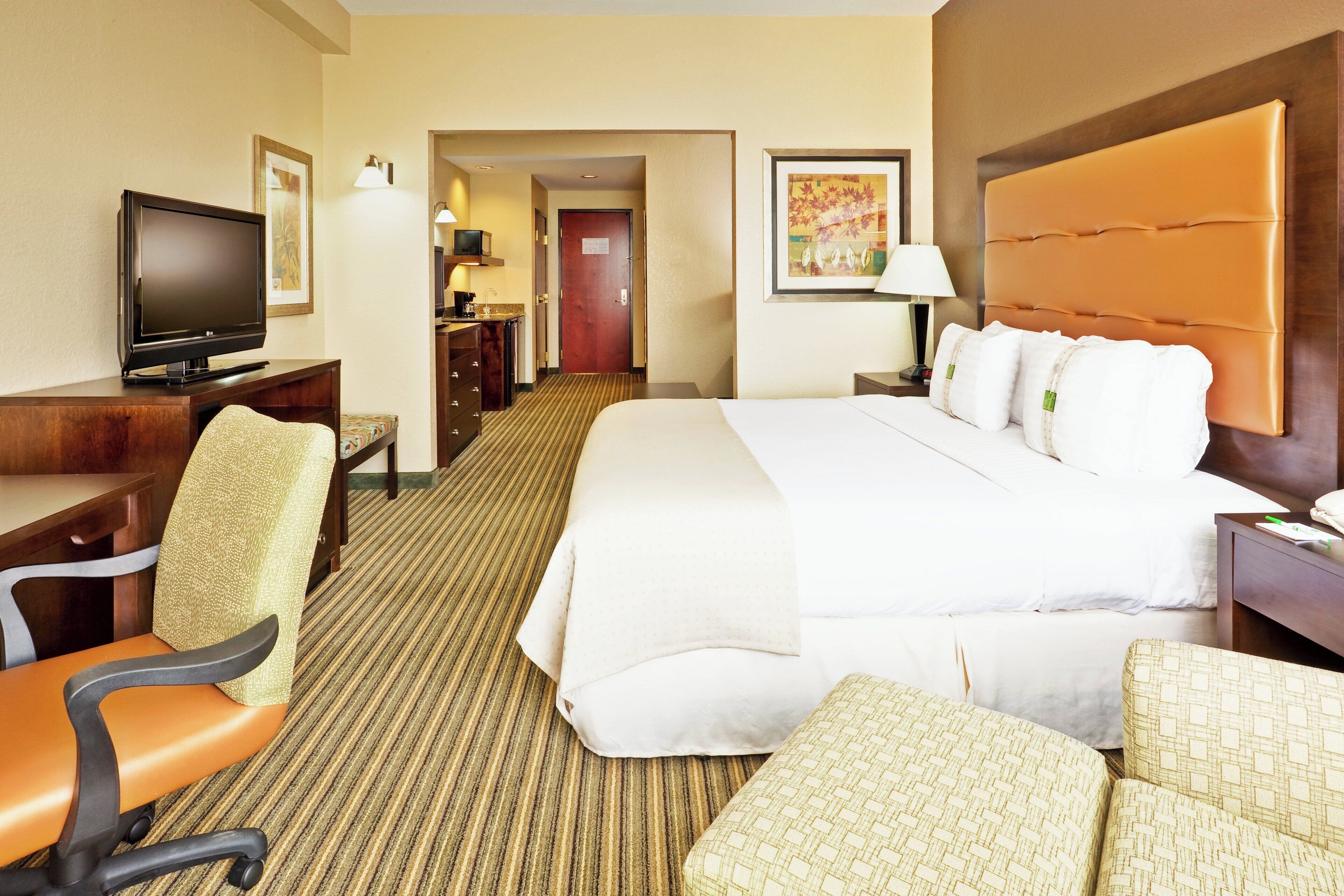 A hotel room with a bed, a desk, a television, a chair, and a carpeted floor.