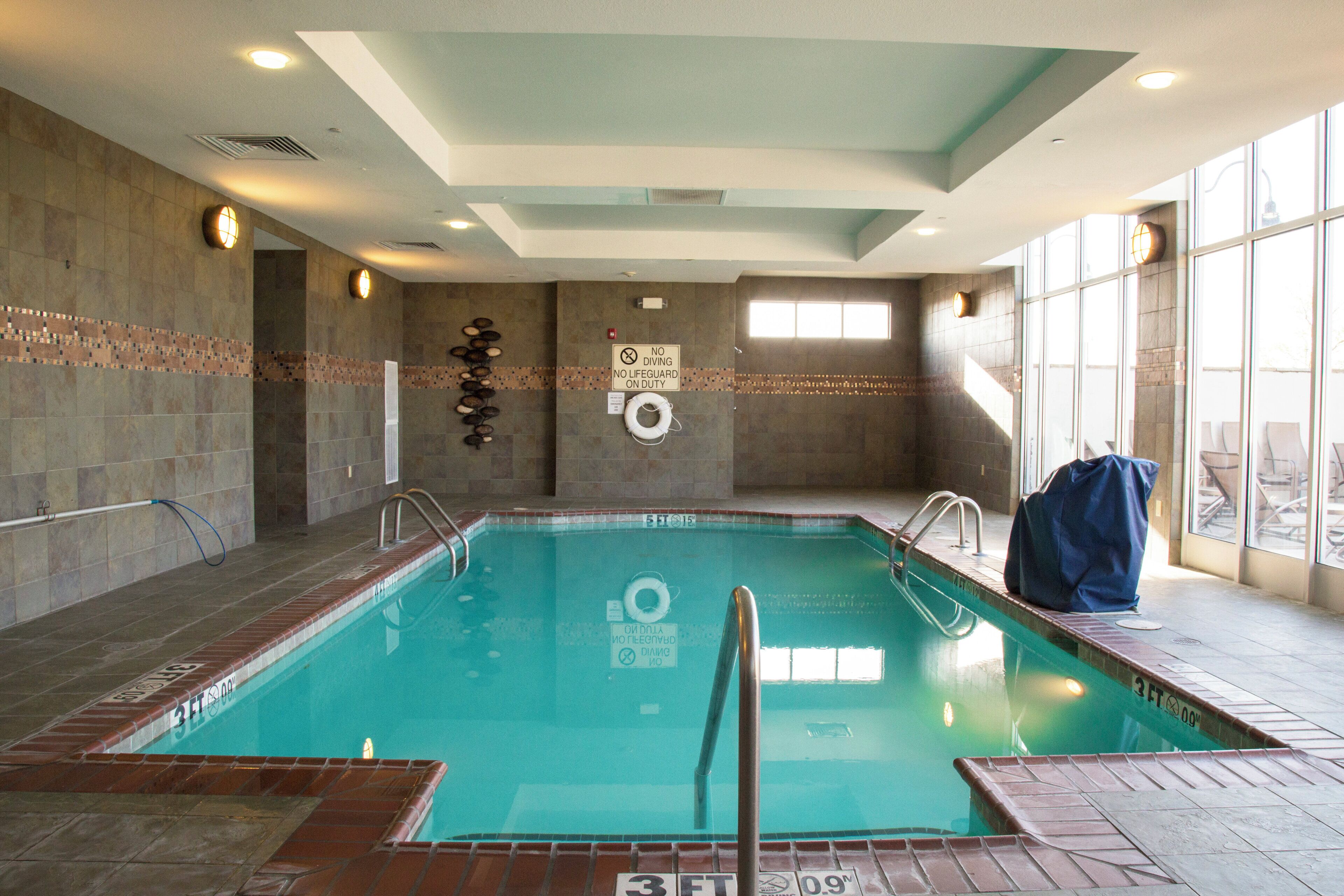 Una piscina interior con agua cristalina, líneas de profundidad marcadas y un cartel de prohibido bucear en la pared.