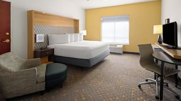 Une chambre d’hôtel équipée d’un lit, d’un bureau avec un ordinateur, d’une chaise, d’une télévision, d’un ventilateur de plafond et d’une fenêtre avec des stores.