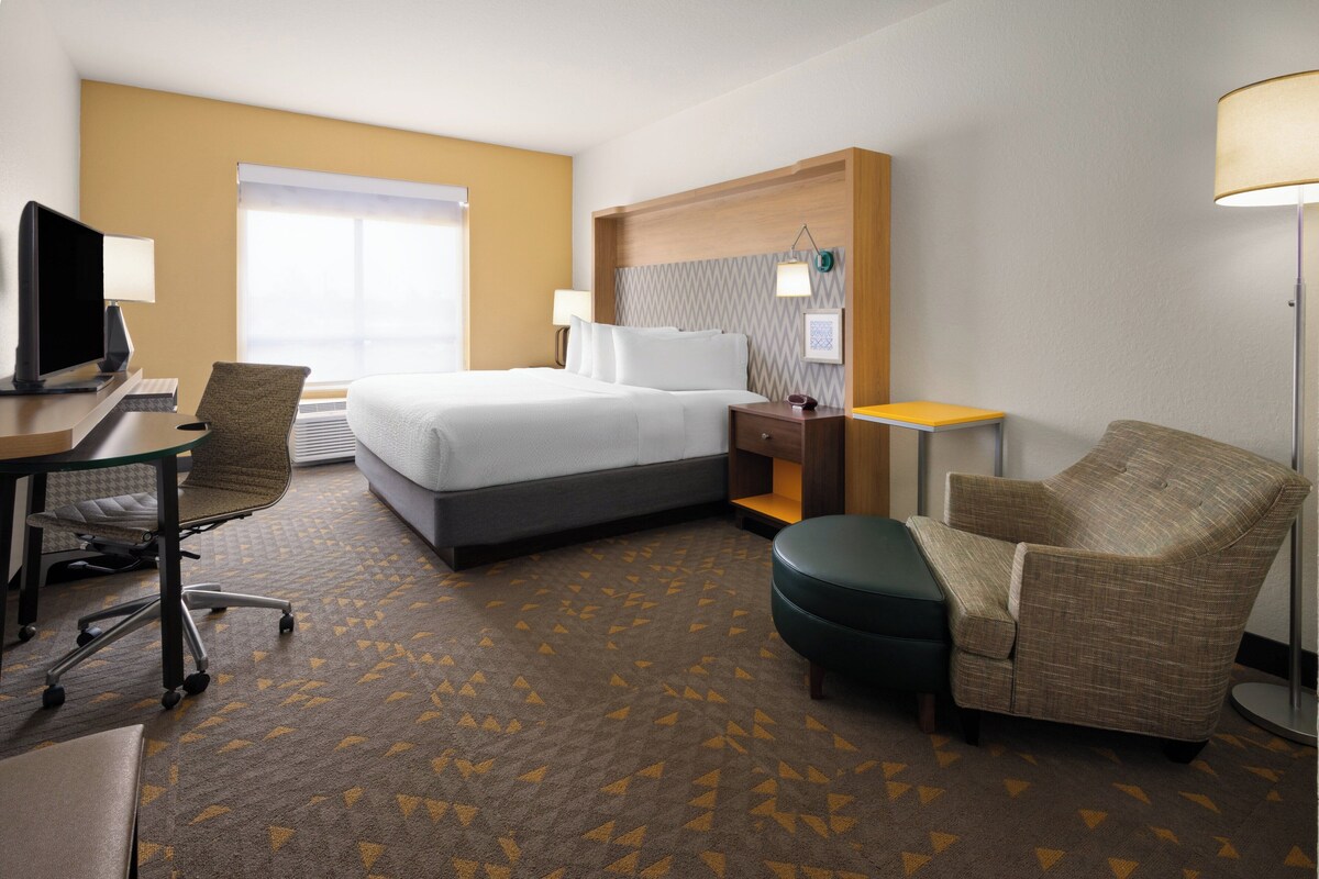 A hotel room with a bed, desk, chair, lamp, and a view of the outdoors.