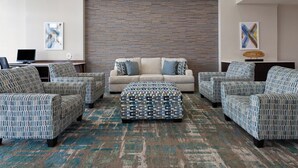 A modern living room with a patterned sofa set, a central ottoman, and a brick-patterned wall. - Holiday Inn Jackson Southeast - Pearl by IHG (Pearl)