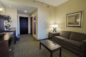A hotel room with a kitchenette, a sofa, a table, and a lamp.