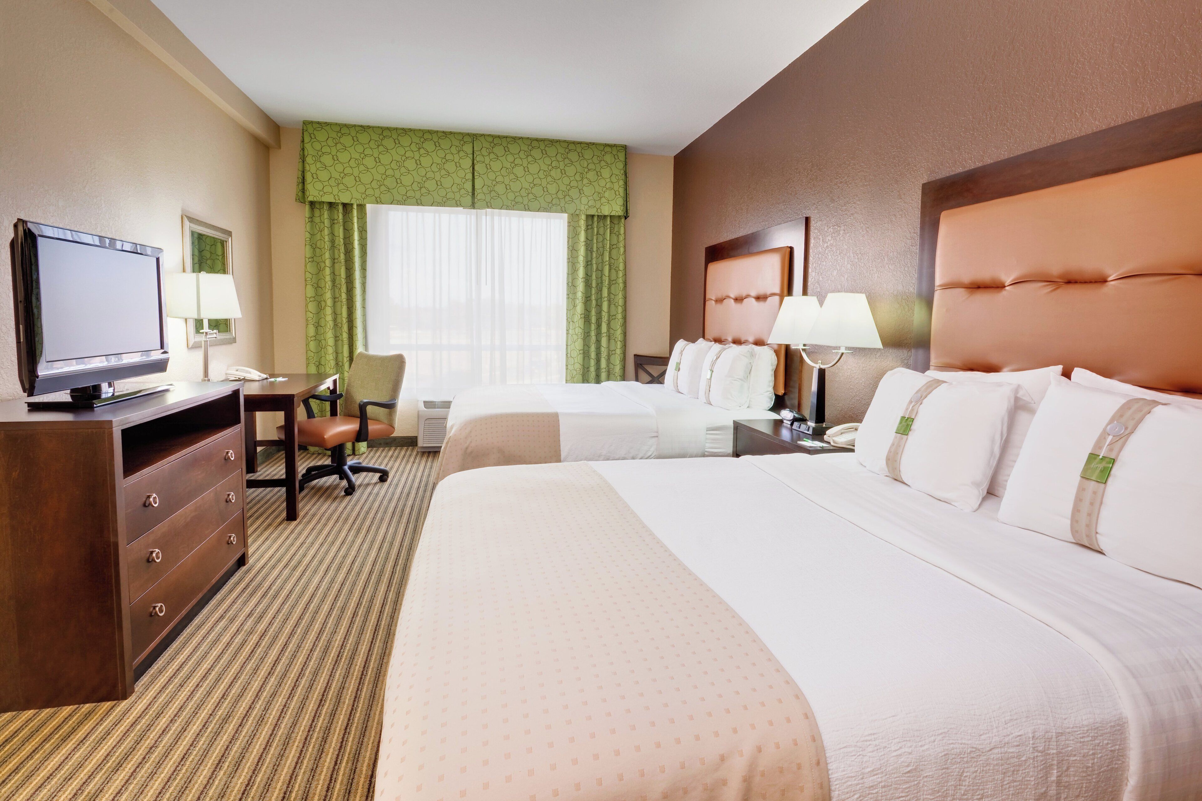 A hotel room with two beds, a desk, a chair, a television, and a window with curtains.