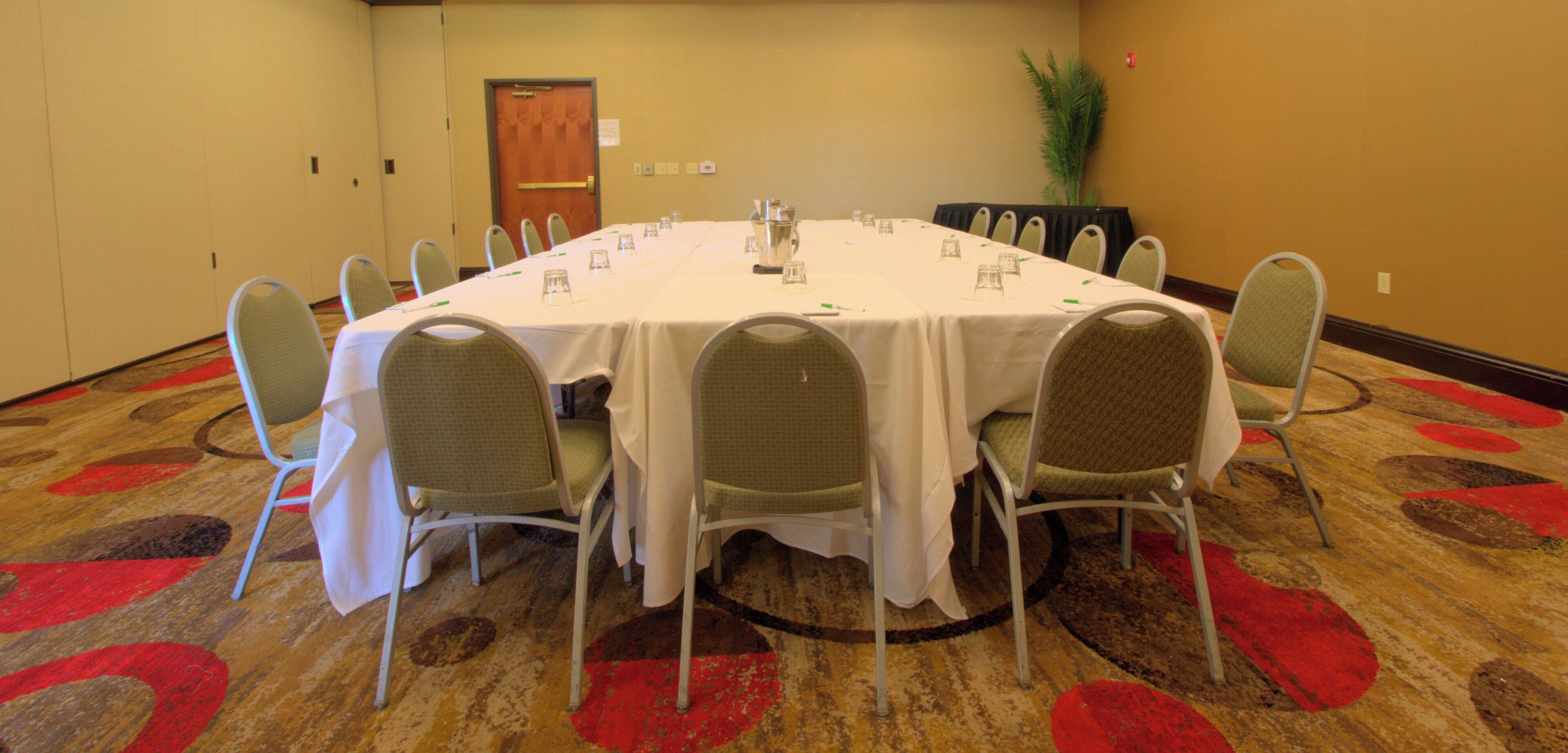 Un salón de conferencias con una mesa rectangular, sillas y piso alfombrado.
