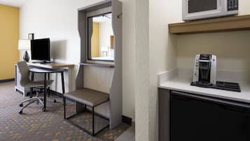 Ein Hotelzimmer mit Schreibtisch, Stuhl, Mikrowelle, Kaffeemaschine und einem kleinen Schrank.