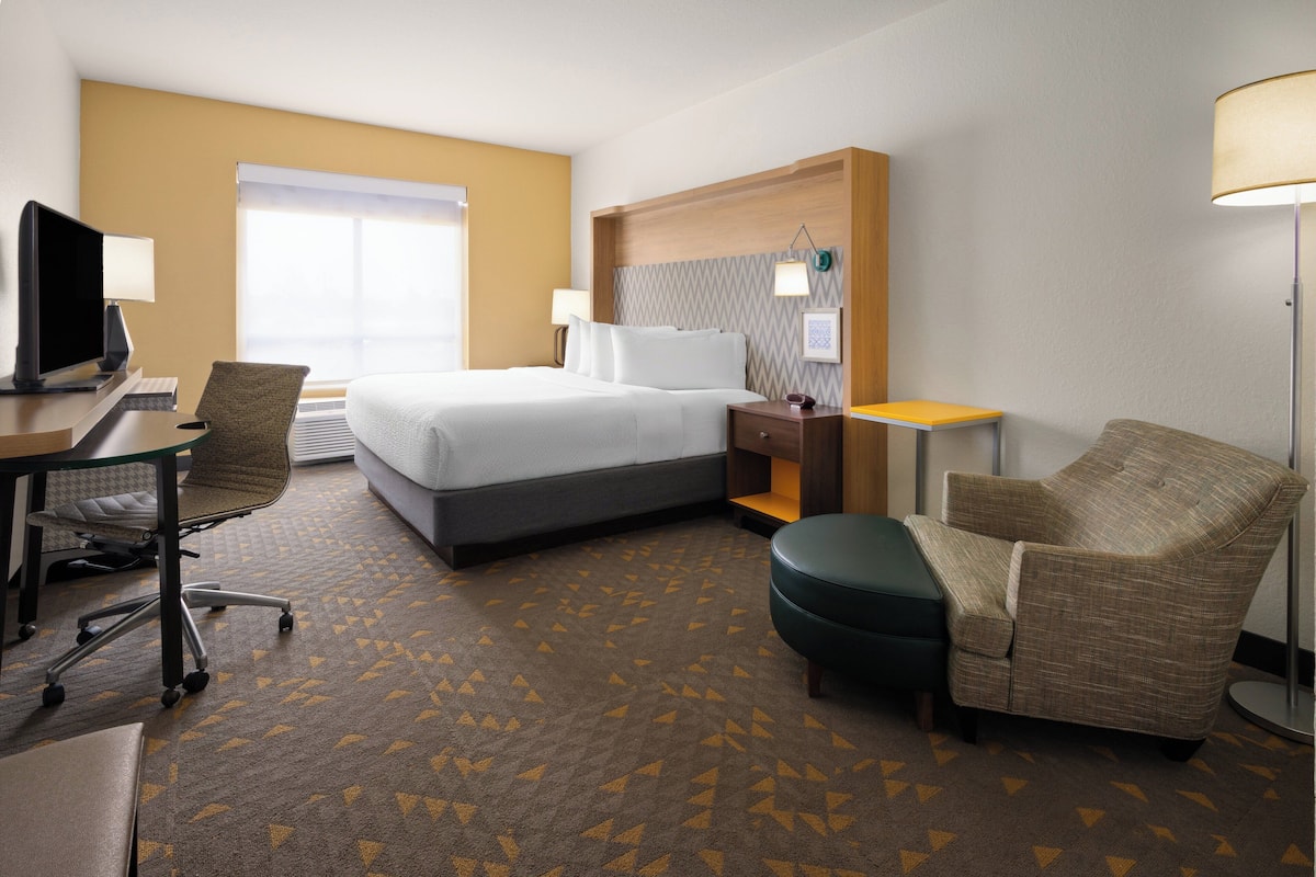A hotel room with a bed, desk, chair, lamp, and a view of the outdoors.