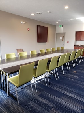A conference room with a long table and yellow chairs, a wooden cabinet, and an exit sign. - Holiday Inn Express & Suites Lincoln Airport by IHG (Lincoln)