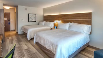 A hotel room with two beds, a wooden headboard, a framed picture on the wall, and a small table with a lamp.